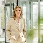 Ulrike Hostehradsky steht am Eingang des MTC an einer Glasdrehtür mit beigefarbenem Blazer